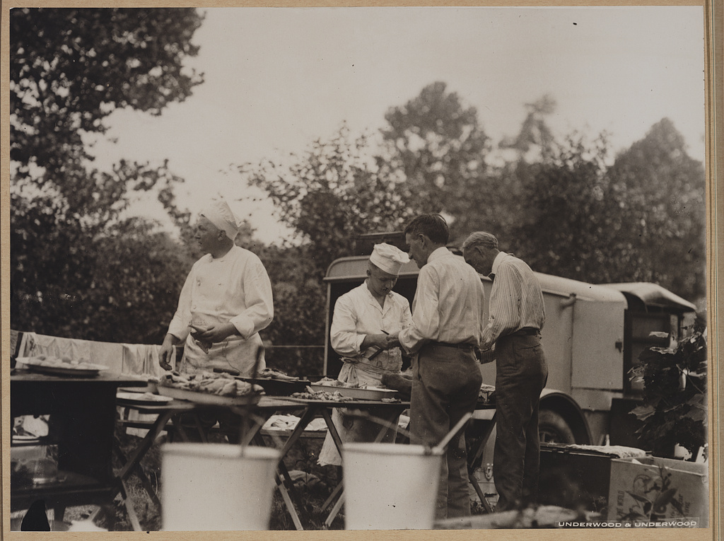 Henry Ford and Harvey Firestone assisting two chefs by peeling potatos at a Ford-Edison camping trip